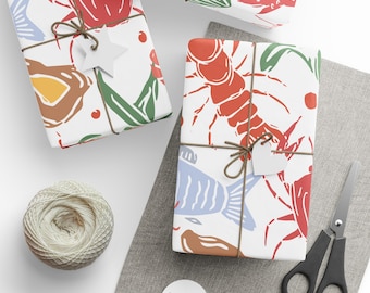May include: Three white gift boxes with a nautical theme. The boxes are decorated with red and blue lobsters, fish, and seaweed. The boxes are tied with twine and have a white tag attached.