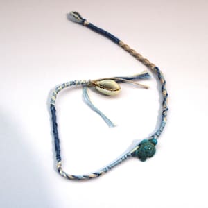 May include: A blue and white braided friendship bracelet with a small white seashell and a turquoise turtle charm.