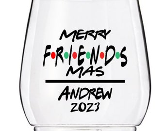 Op de afbeelding: Helder glazen wijnglas met de tekst "Merry Friendsmas Andrew 2023" in zwarte letters met rode, groene en witte stippen.