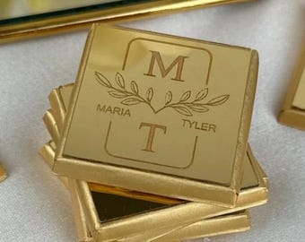 Puede incluir: Una pila de posavasos cuadrados de metal dorado con acabado reflectante. El posavasos superior presenta un diseño grabado con la letra M sobre un motivo de rama frondosa, el nombre Maria, el nombre Tyler y la letra T dentro de un borde fino.