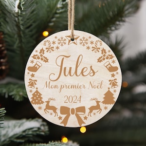 Peut inclure: Une décoration de Noël ronde en bois avec un motif gravé brun. L'ornement présente le nom "Jules", le texte "Mon premier Noël" et l'année "2024".