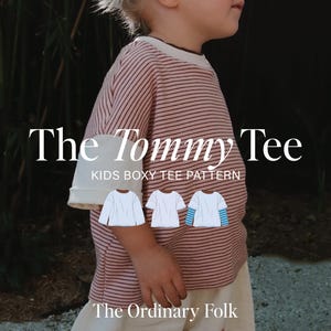 Può includere: Una t-shirt dal taglio squadrato con sottili righe orizzontali in un colore bruno-rossastro tenue. Il testo recita The Tommy Tee KIDS BOXY TEE PATTERN e The Ordinary Folk. Tre piccoli disegni a linee bianche mostrano varianti di maniche.