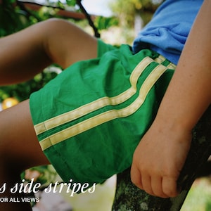 May include: Bright green athletic shorts featuring two parallel light yellow stripes running down the side. The shorts are paired with a plain blue t-shirt. The text Bias side stripes OPTION FOR ALL VIEWS is printed in white at the bottom.