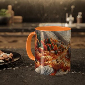 May include: Orange ceramic mug with a fall-themed design. The mug features a landscape with pumpkins, trees, and a house. The interior and handle are solid orange. Steam rises from the mug, suggesting a warm beverage.