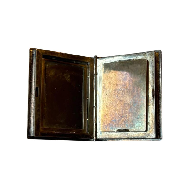 Puede incluir: Un pitillera de plata antigua, abierta. La pitillera es rectangular con tapa abisagrada e interior deslustrado. El metal tiene un aspecto desgastado y vintage, con signos visibles de edad y uso. La pitillera est&aacute; vac&iacute;a.