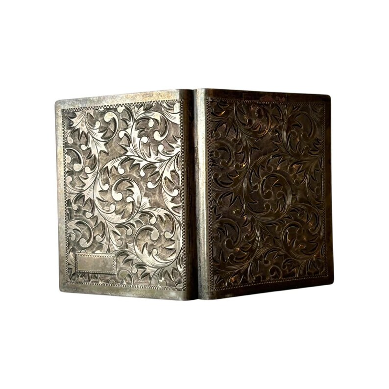 Puede incluir: Una caja rectangular plateada con un patr&oacute;n floral ornamentado grabado en su superficie. La caja est&aacute; abierta, revelando su interior. El intrincado dise&ntilde;o cubre toda la superficie, creando una est&eacute;tica vintage.
