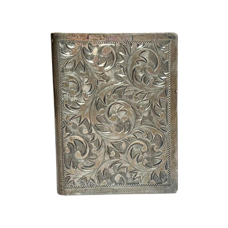 Puede incluir: Un estuche rectangular de metal plateado con un patr&oacute;n floral grabado y ornamentado. El dise&ntilde;o presenta hojas y vides arremolinadas, con un borde texturizado. El estuche parece ser vintage o antiguo.