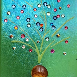 May include: A decorative night light featuring a tree design with colorful accents. The artwork has a green and blue background with a brown sphere at the base and colorful gems. The night light is rectangular and has a white plug-in base.