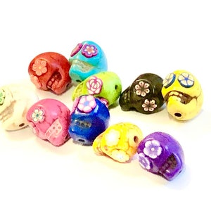 May include: A collection of 12 colorful skull beads with floral designs. The beads are made of ceramic and are approximately 1 inch in size. They are perfect for making jewelry or other crafts.