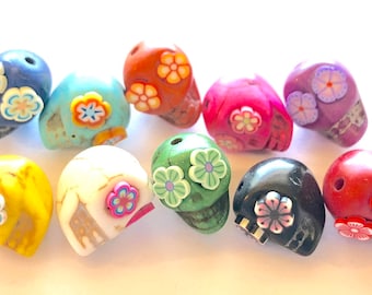 May include: A collection of ten colorful skull beads with floral designs. The beads are made of various materials, including painted wood, plastic, and resin. Each bead features a different color and floral pattern.