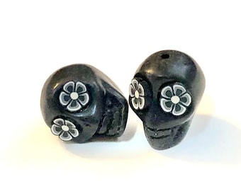 May include: Two black ceramic skull beads with white flower designs. The skulls have a hole at the top for stringing.