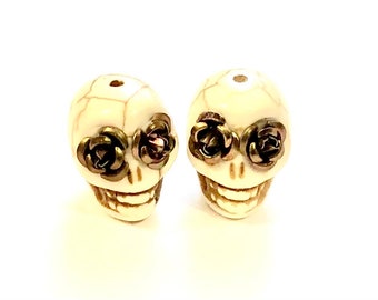 May include: Two white skull beads with gold rose accents. The beads are approximately 1 inch in diameter and have a detailed skull design.