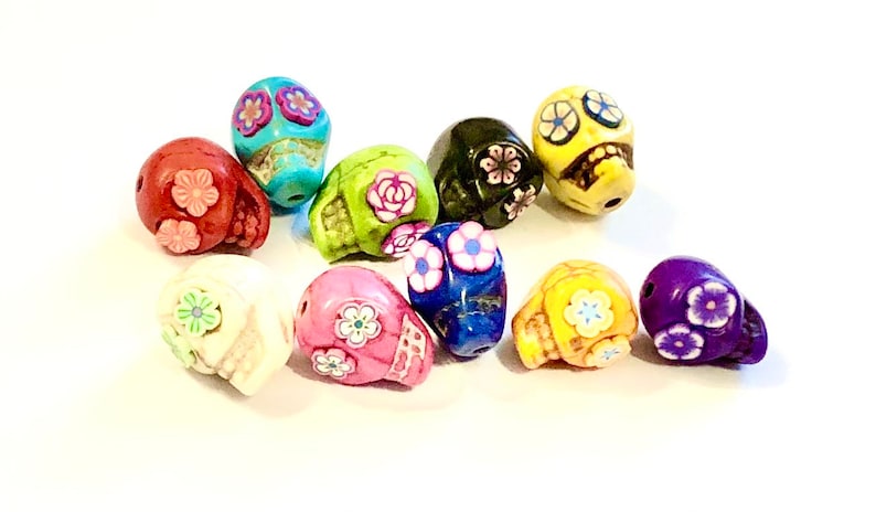May include: A collection of ten colorful skull beads with floral designs. The beads are made of ceramic and have a glossy finish. The colors include red, white, green, blue, yellow, and purple.