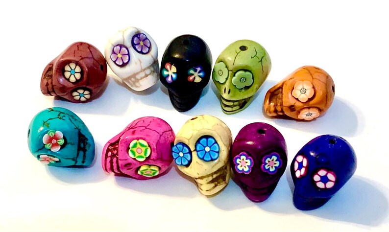 May include: Ten colorful skull beads with floral designs. The beads are made of ceramic and have a variety of colors, including turquoise, pink, purple, green, and white.