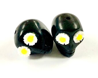 May include: Two black skull beads with white daisy flowers for the eyes. The beads are about 1 inch in diameter.