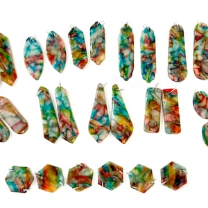 May include: A collection of multicolored acrylic jewelry pendants in various geometric shapes including hexagons, ovals, and elongated forms. Each piece features a marbled pattern with swirls of blue, red, yellow, and white, all with small silver jump rings.