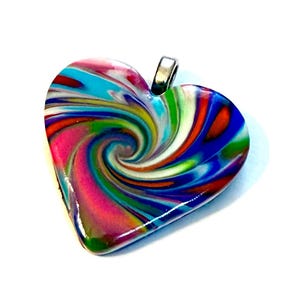 May include: A heart-shaped pendant with a swirling pattern of vibrant colors including pink, blue, green, and orange. The pendant has a silver-colored bail for attaching to a chain. The design resembles a colorful candy swirl.