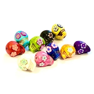 May include: Assortment of colorful skull beads with floral designs. The beads are made of ceramic and have a glossy finish. The colors include red, green, blue, yellow, purple, white, and black.