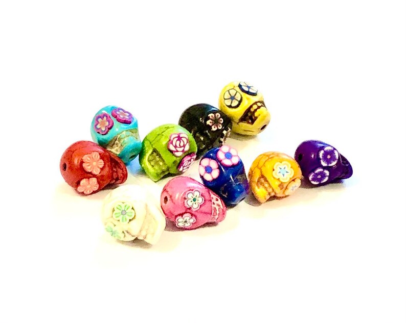 May include: Assortment of colorful skull beads with floral designs. The beads are made of ceramic and have a glossy finish. The colors include red, green, blue, yellow, purple, white, and black.