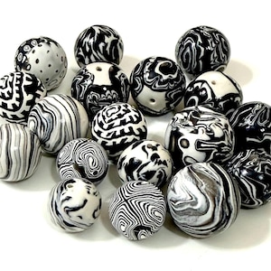 May include: A collection of spherical beads featuring various black and white marbled, swirled, and geometric patterns. Each bead has a smooth, polished surface with distinct, high-contrast designs, including concentric lines, organic shapes, and dots.