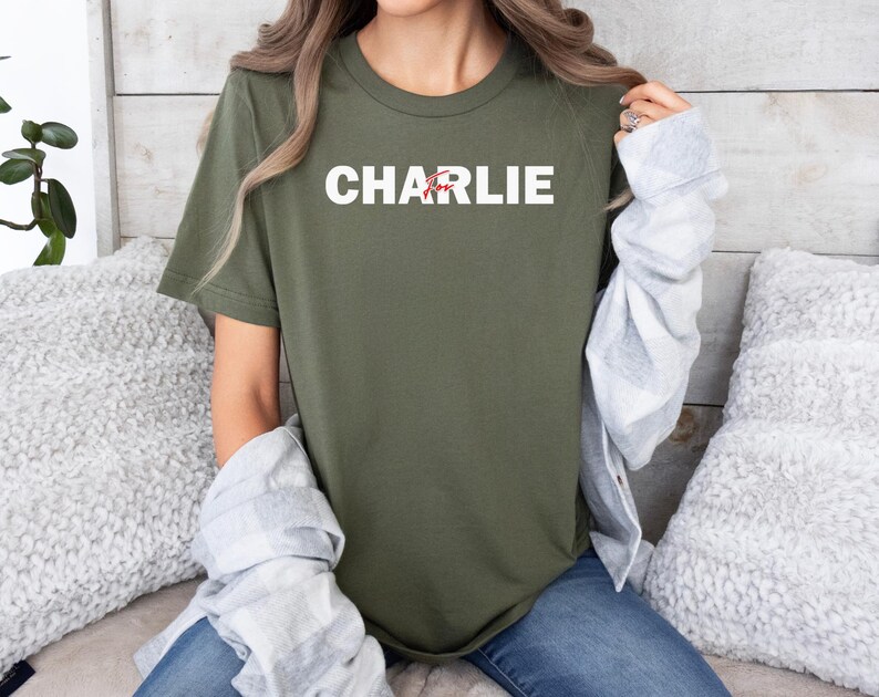 A person wearing a green t-shirt with the name "CHARLIE" printed on it, sitting on a couch with a gray sweater draped over their arm.