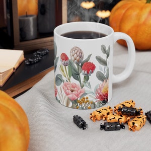 May include: White ceramic mug with a floral design featuring pink, red, and green flowers. The mug is filled with coffee and steam is rising from the top.