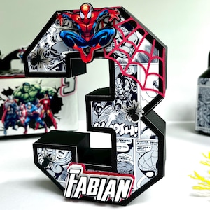 May include: Black and red 3D number three with a Spiderman comic book theme. The number is decorated with images of Spiderman, Hulk, Iron Man, and other Marvel characters. The number is personalized with the name "FABIAN".