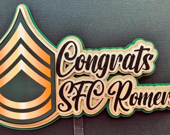 May include: A green and gold cake topper with a black and gold chevron design and the text "Congrats SFC Romero".