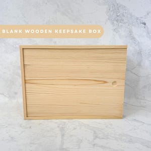 May include: A rectangular, blank wooden keepsake box with a light wood grain finish. The box has a simple, clean design with a lid that fits flush. The text "BLANK WOODEN KEEPSAKE BOX" is displayed in a light beige banner above the box.