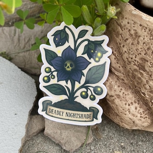 May include: A sticker featuring a stylized illustration of a Deadly Nightshade plant. The design includes a dark blue flower with a skull center, dark green leaves, and the text "Deadly Nightshade" on a banner.