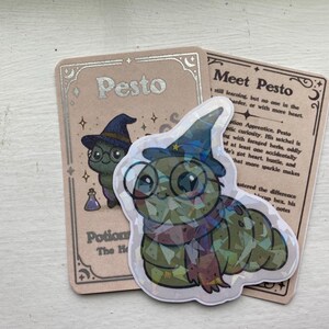 May include: A holographic sticker of a caterpillar wearing a wizard hat, glasses, and a scarf, with the text "Pesto" and "Potion The Healer" on a card. Another card reads "Meet Pesto".
