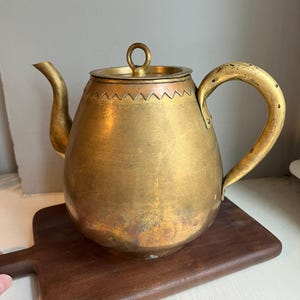 May include: A brass teapot with a copper band around the top. The teapot has a rounded body and a curved handle.