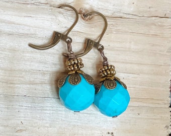 May include: A pair of turquoise blue earrings with gold-toned metal accents. The earrings feature a faceted round bead and a decorative flower-shaped charm.