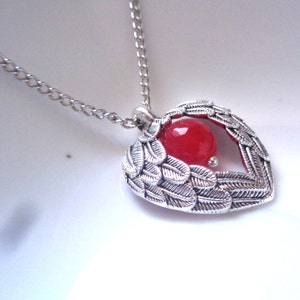May include: Silver heart pendant necklace with a red gemstone inside. The heart is adorned with detailed silver wings.