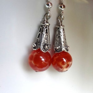 May include: A pair of dangle earrings with orange and white marbled glass beads and silver filigree accents.
