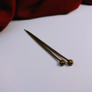 May include: Two gold-toned hair sticks with a diamond-shaped design at the end.