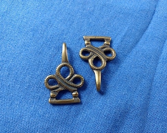 May include: Two antique gold-toned metal buckles with an intricate knot design. The buckles have a loop on one end and a hook on the other.