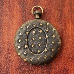 May include: A vintage pocket watch with a gold-toned finish and a star pattern on the face. The watch has a hinged lid and a decorative ring.