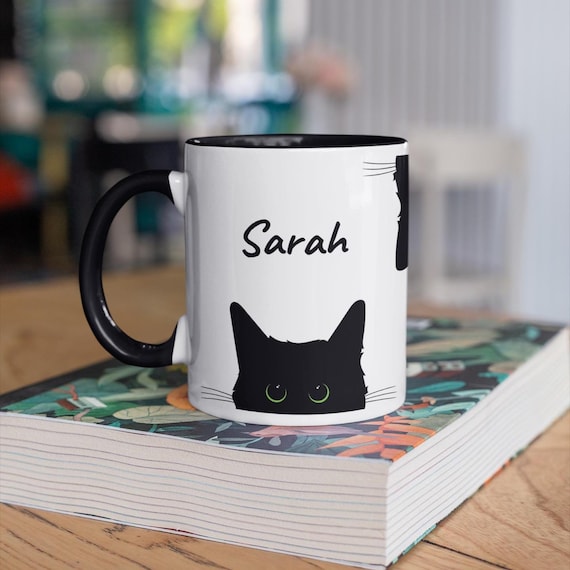 A personalized 11 oz ceramic mug with a playful peeking black cat. Dishwasher & microwave safe. Perfect for cat lovers—choice of eye color.