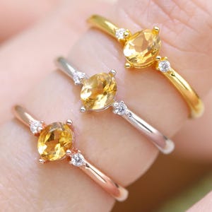 Peut inclure: Trois bagues avec des pierres précieuses ovales jaunes et de petites pierres claires. Les bagues sont en or, argent et or rose. Les bagues sont présentées sur un doigt, mettant en valeur les différentes couleurs de métal.