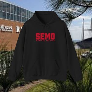 Może przedstawiać: Czarna bluza z kapturem z przednią kieszenią i sznurkiem. Bluza ma czerwony napis "SEMO" nad "MUSICAL THEATRE". Tło obejmuje budynek i drzewa.