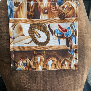 closeup of the western horse tote bag outside pocket with a ranch and horses in the background.