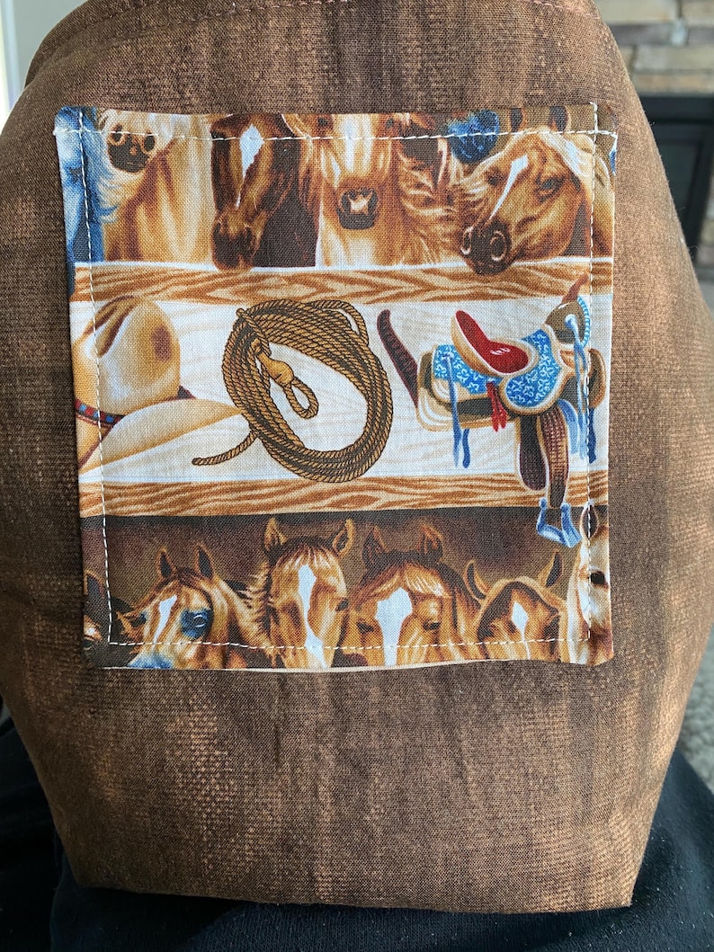 closeup of the western horse tote bag outside pocket with a ranch and horses in the background.