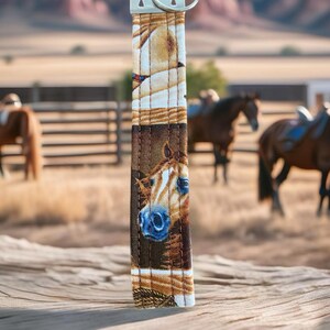 closeup of a key wristlet with horse themed fabric with a ranch and horses in the background.