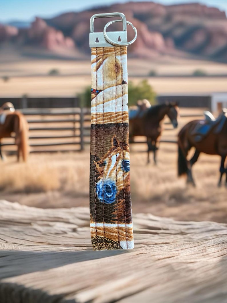closeup of a key wristlet with horse themed fabric with a ranch and horses in the background.