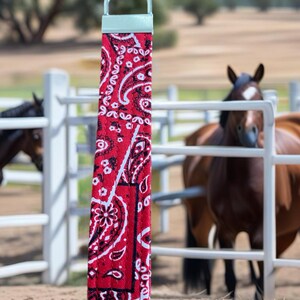 closeup of a red bandana key wristlet horses behind a closed gate in the background.