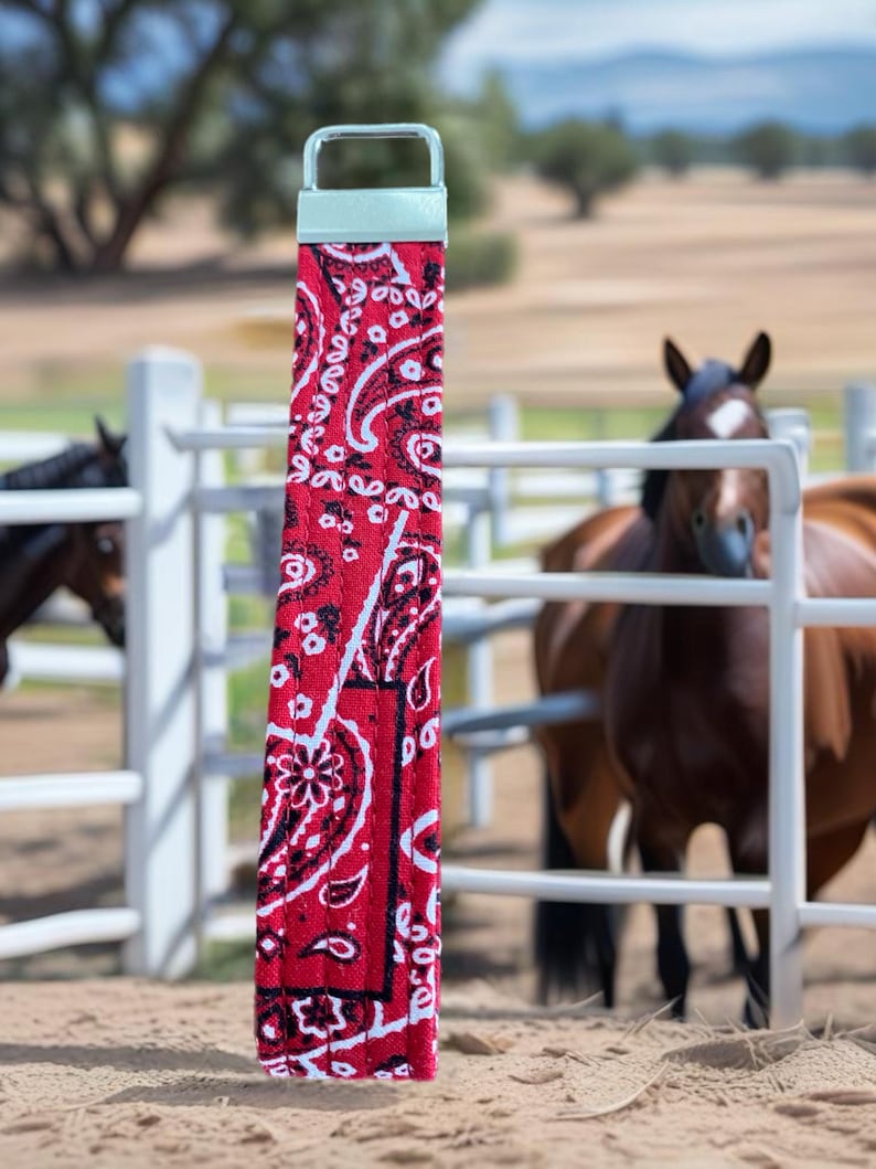 closeup of a red bandana key wristlet horses behind a closed gate in the background.