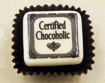 May include: A white chocolate square with a black border and the text "Certified Chocoholic" in black lettering. The chocolate is in a black paper wrapper.