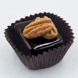 Puede incluir: Una sola trufa de chocolate cubierta con una nuez de pec&aacute;n, en un vaso de papel marr&oacute;n.