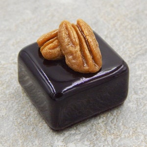 Puede incluir: Un peque&ntilde;o pastel cuadrado de chocolate negro cubierto con dos mitades de nuez pecana.